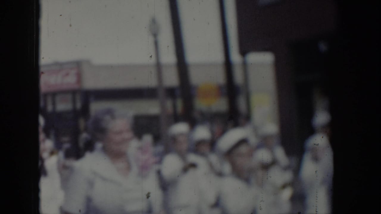 Uniformed marchers in white with white-brimmed caps during a 1965 Saint Louis civic parade, with commercial storefronts lining the street behind them