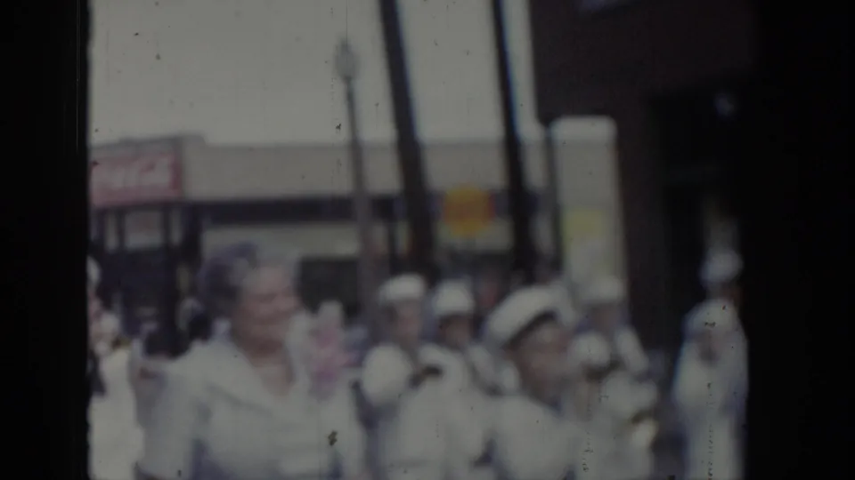 Uniformed marchers in white with white-brimmed caps during a 1965 Saint Louis civic parade, with commercial storefronts lining the street behind them