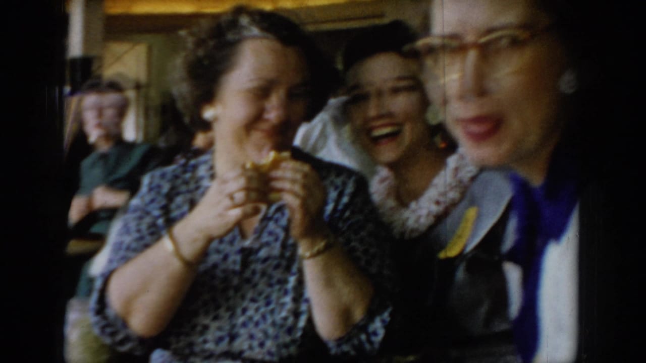 Close-up of two women laughing; a third woman in cat-eye glasses and blue outfit partially visible at frame right.