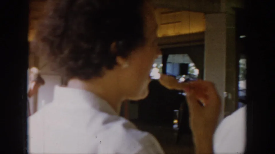 A woman in a white outfit, possibly dining, seen from behind and in profile in a mid-1960s restaurant interior circa 1965.