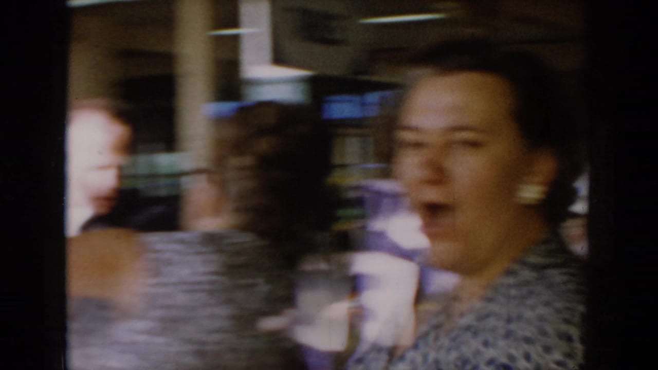Close-up of a woman mid-expression, mouth open, wearing a patterned top, captured with motion blur in 8mm at a 1960s dining venue.