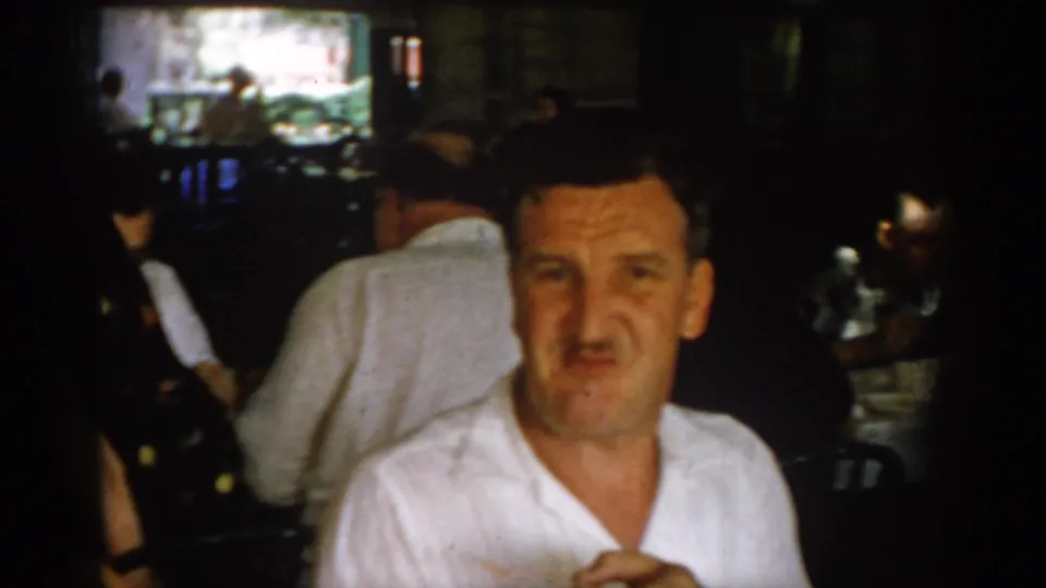 Close-up of a middle-aged man in a white short-sleeve shirt seated in what appears to be a covered patio restaurant, circa 1965 Saint Louis.