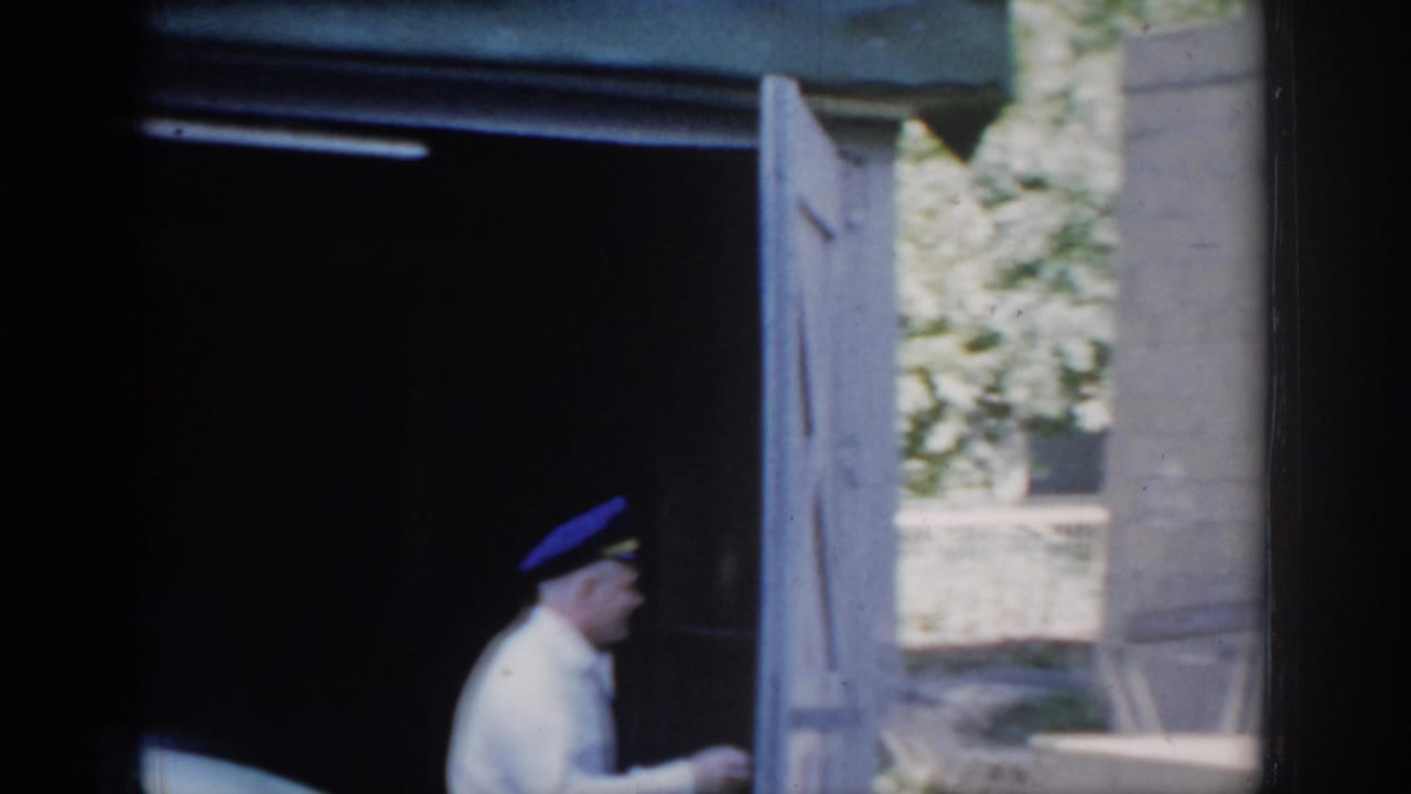 Older man in white service uniform and blue peaked cap pushing open a painted blue garage door; Saint Louis, Missouri, circa 1965, 8mm home movie.