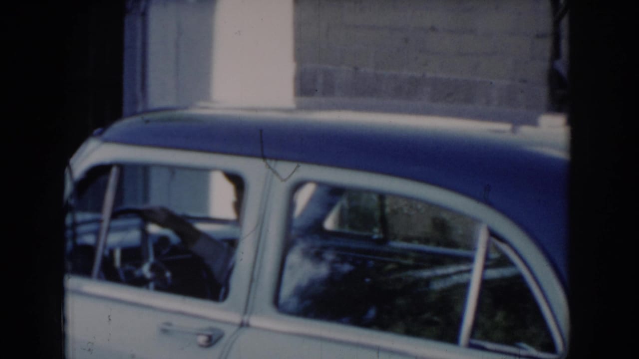 Side profile of a two-tone blue and white 1960s American sedan; man at the steering wheel, brick wall behind — Saint Louis, Missouri, circa 1965.