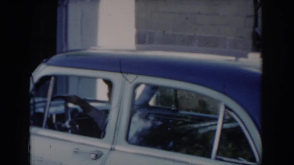 Side profile of a two-tone blue and white 1960s American sedan; man at the steering wheel, brick wall behind — Saint Louis, Missouri, circa 1965.