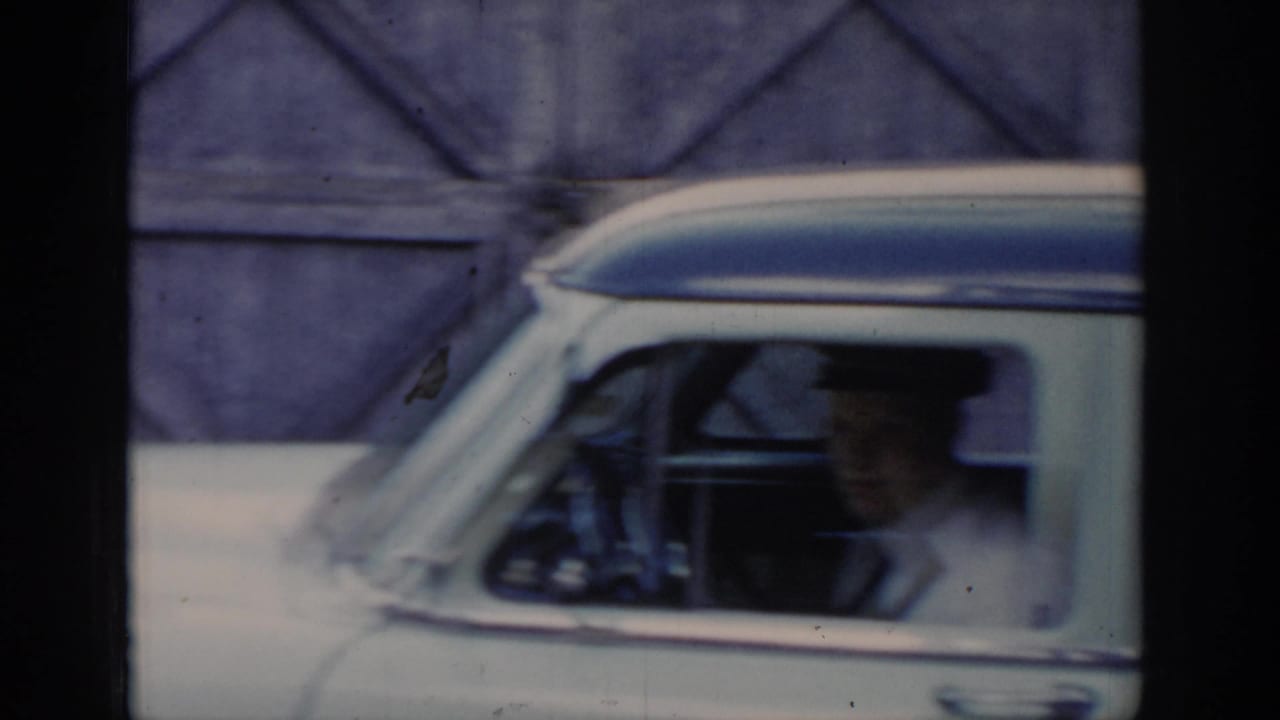 8mm footage of a white-and-blue mid-century American taxi seen from outside, with a uniformed capped figure visible through the side window, circa 1965 Saint Louis.
