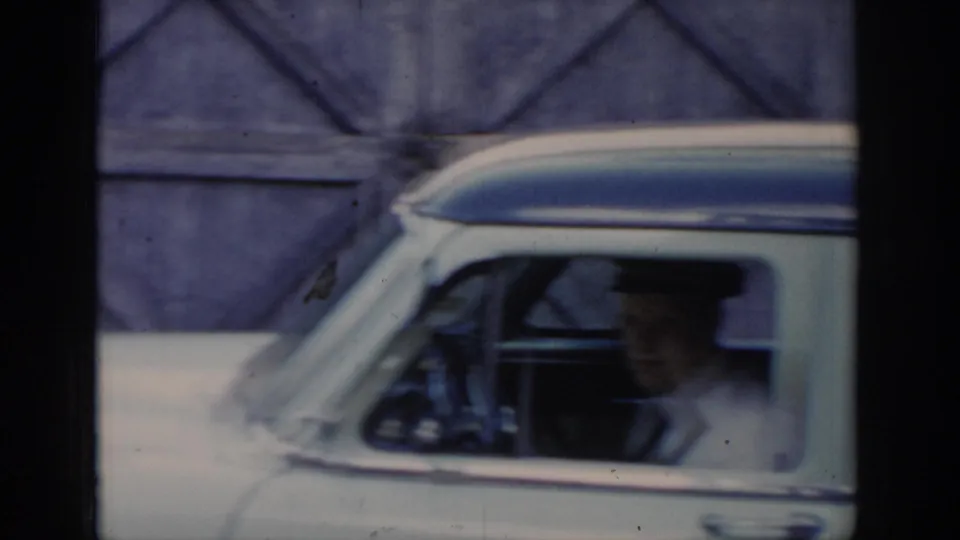 8mm footage of a white-and-blue mid-century American taxi seen from outside, with a uniformed capped figure visible through the side window, circa 1965 Saint Louis.