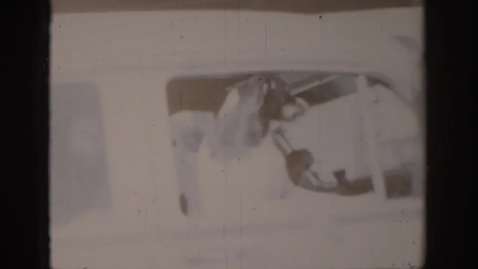 Severely overexposed and faded 8mm frame showing a dog through or near a vehicle window; emulsion loss renders most detail illegible, circa 1965.