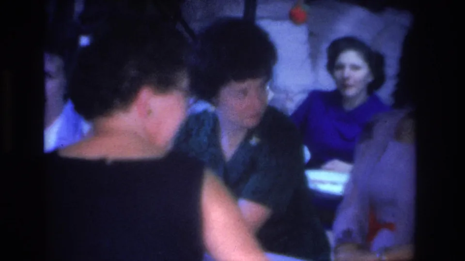 Group of women in mid-1960s dress gathered at a table during an evening social event, Hoboken, New Jersey, circa 1966, shot on 8mm film.