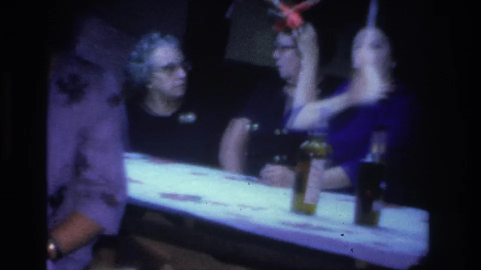 Women including a gray-haired woman with glasses seated at a table with small bottles or glasses, at an evening social gathering, circa 1966.