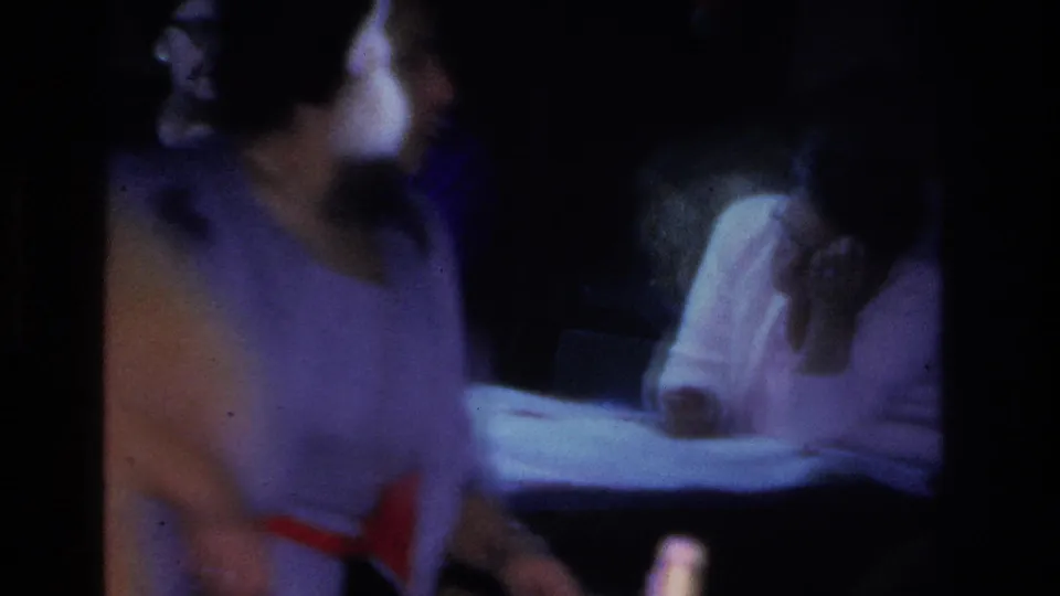 Close, motion-blurred handheld shot of women at an evening social, circa 1966; strong blue cast and blur convey 8mm home-movie character.