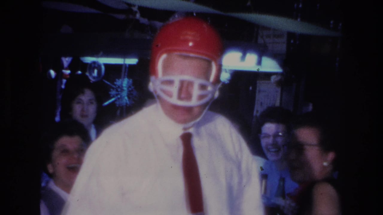 Man wearing a red football helmet as a party novelty at a 1966 indoor gathering in Hoboken, New Jersey; laughing female guests and sparkly hanging decorations visible in the background.
