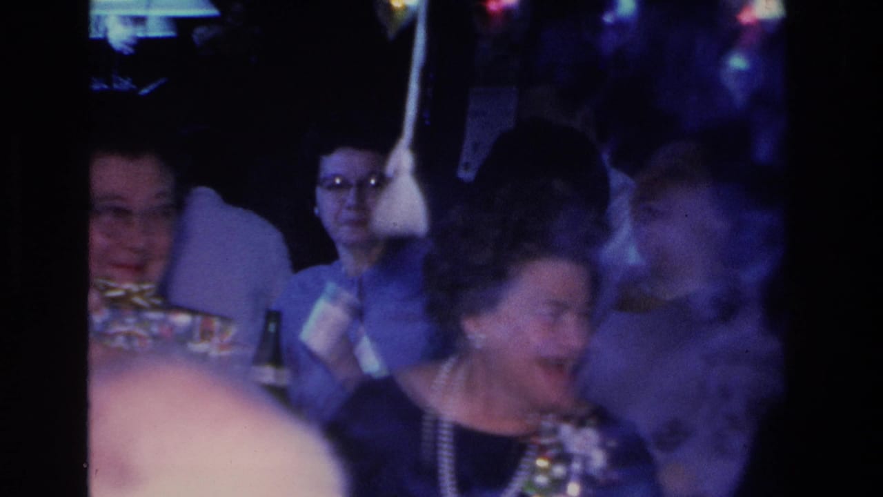 Two women at an indoor party — one wearing eyeglasses on the left, another with a pearl necklace laughing on the right.