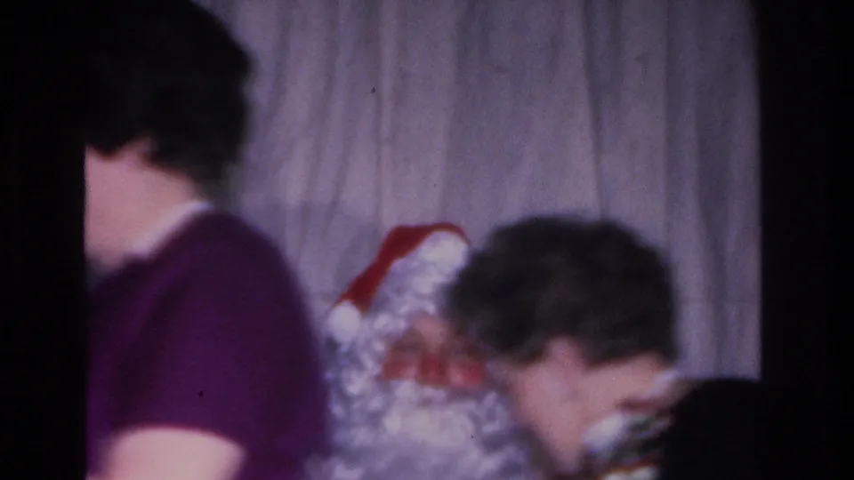 Adults at a 1966 Hoboken, NJ Christmas gathering seen from behind; Santa Claus figure with red hat and white beard occupies foreground, 8mm film.