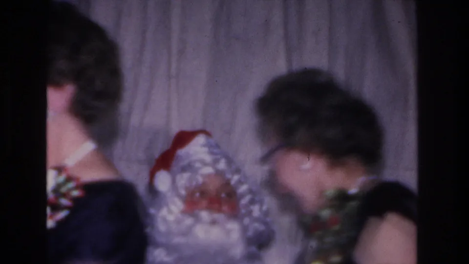 Adults at a 1966 Hoboken, NJ Christmas gathering; Santa figure with red hat and a striped wrapped gift appear in the lower portion of a close handheld 8mm shot.