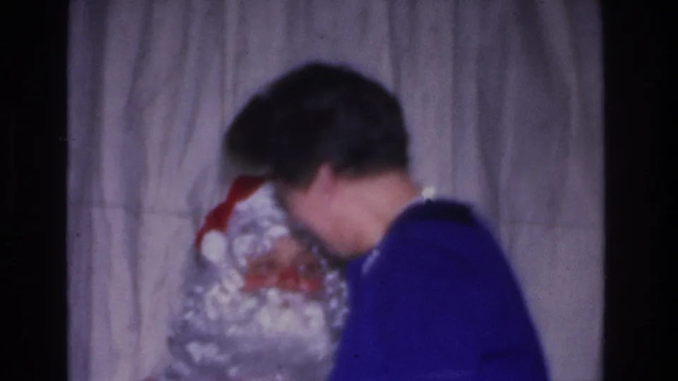 Woman in blue sweater leaning toward a Santa Claus figure, 8mm home movie, mid-1960s indoor holiday gathering, Hoboken New Jersey