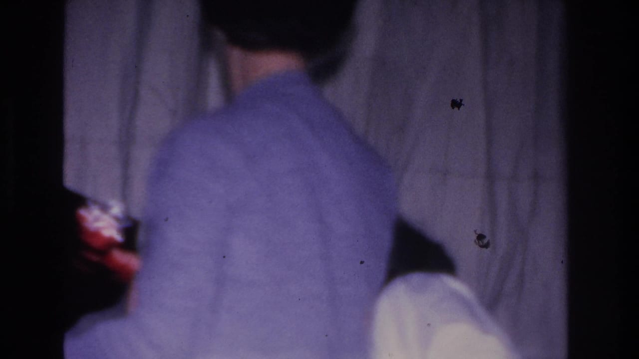 Same adult in light-blue sweater viewed from directly behind; white curtain backdrop; red costume visible at center-right edge.