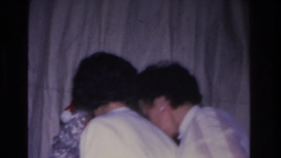 Two adults in white clothing filmed from behind as they interact with Santa Claus at a 1966 Hoboken, NJ holiday gathering; red costume and white beard visible at frame edge.