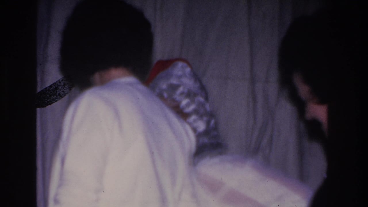 8mm home movie frame, c. 1966; woman seen from behind near Santa Claus at an indoor holiday gathering in Hoboken, New Jersey.