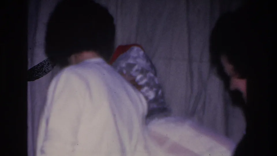 8mm home movie frame, c. 1966; woman seen from behind near Santa Claus at an indoor holiday gathering in Hoboken, New Jersey.