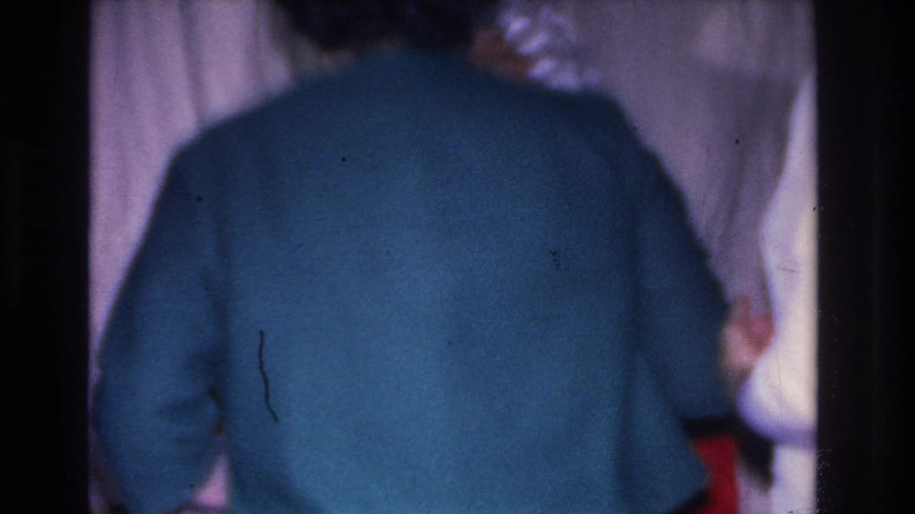 Woman in a teal sweater, back to camera, stands near a Santa Claus figure in a domestic interior; 8mm footage, Hoboken, New Jersey, circa 1966.