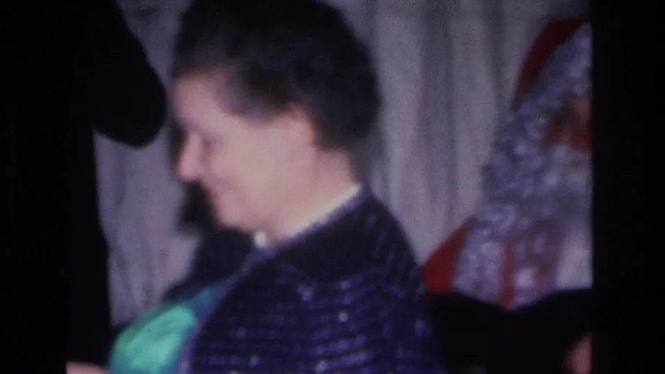 Woman in a dark patterned jacket in profile near a Santa Claus figure; 8mm home movie footage, Hoboken, New Jersey, circa 1966.