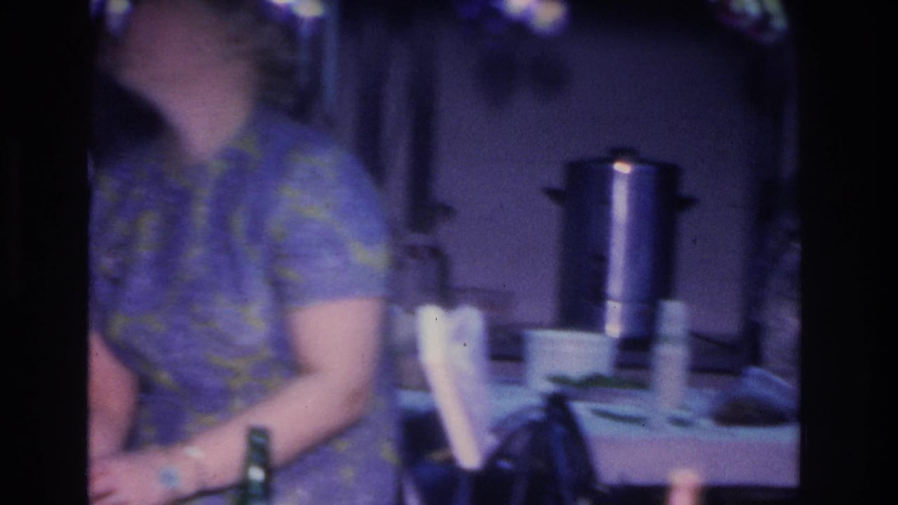 A woman in a mid-1960s patterned shift dress at a party table; a large metal percolator and party supplies are visible in the background of this 1966 8mm home movie from Hoboken, New Jersey.