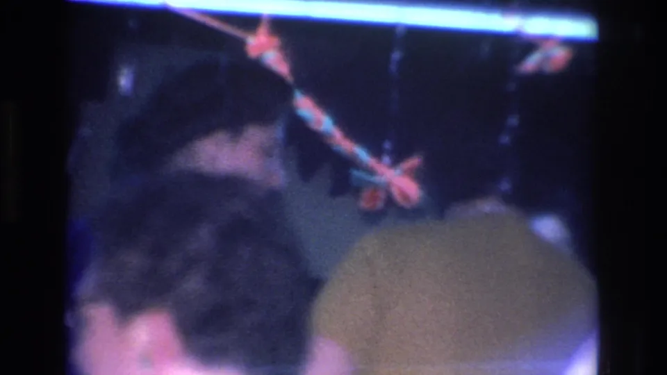 8mm home movie frame, circa 1966, camera shifted to reveal another guest's back with a bright overhead light streak and apparent decorative elements; indoor social gathering, Hoboken, New Jersey.