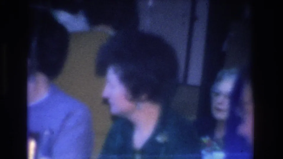 Adult women with 1960s short hairstyles in profile and near-profile indoors on 8mm film; yellow-gold background wall; Hoboken, New Jersey, circa 1966.
