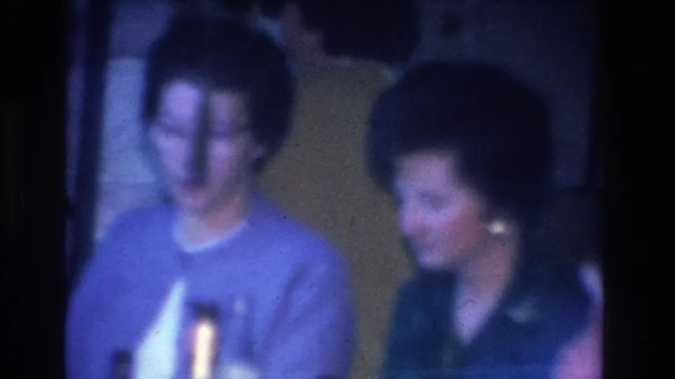 Adult women in a mid-1960s indoor social gathering; light blue sweater prominent in foreground; 8mm blue-purple film cast; Hoboken, New Jersey, circa 1966.