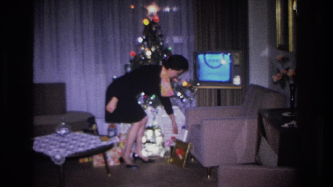 Woman in black dress bending to retrieve a wrapped gift from under a decorated Christmas tree in a mid-1960s American living room.