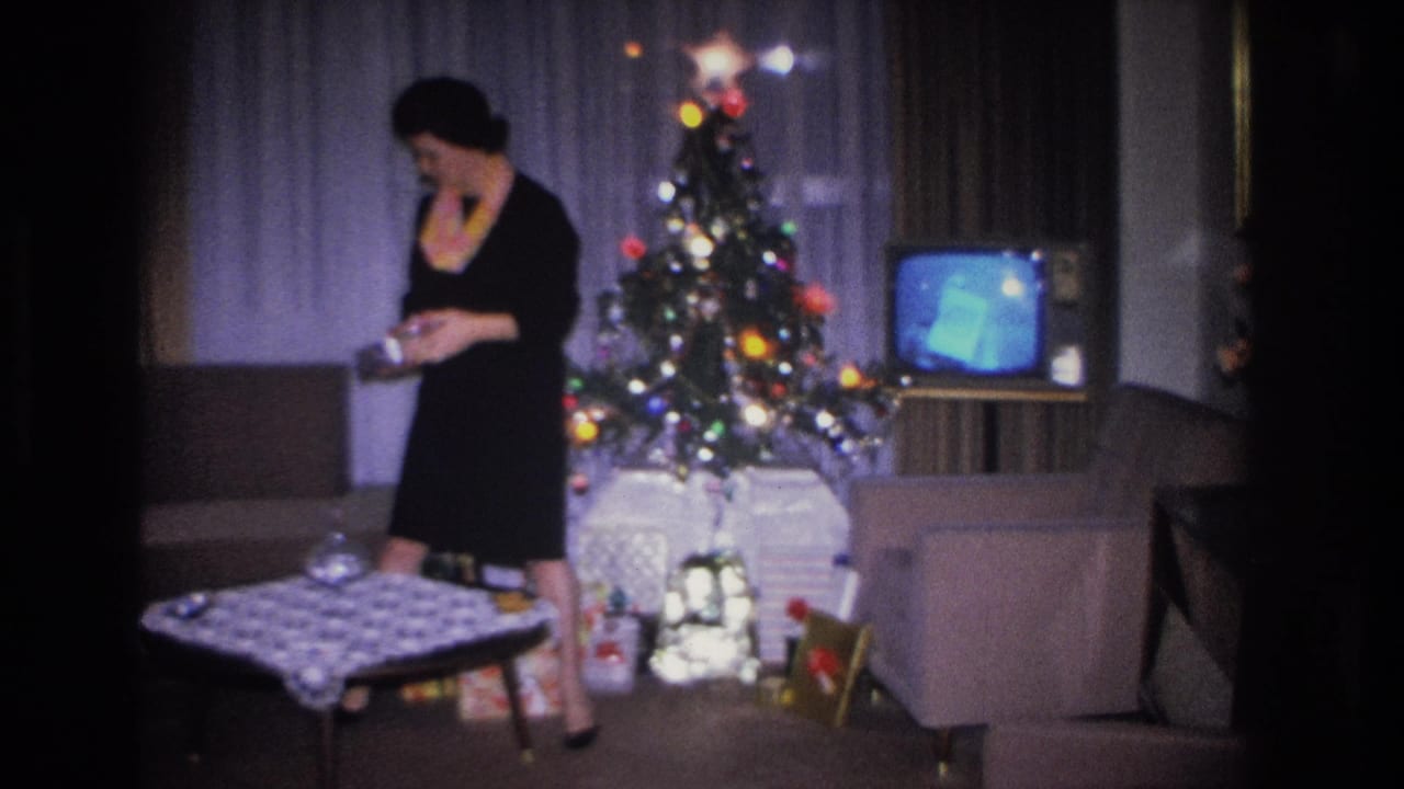 Woman in black dress and colorful scarf stands beside a decorated Christmas tree in a mid-century living room, c.1966 Hoboken, New Jersey, holding an unwrapped gift.