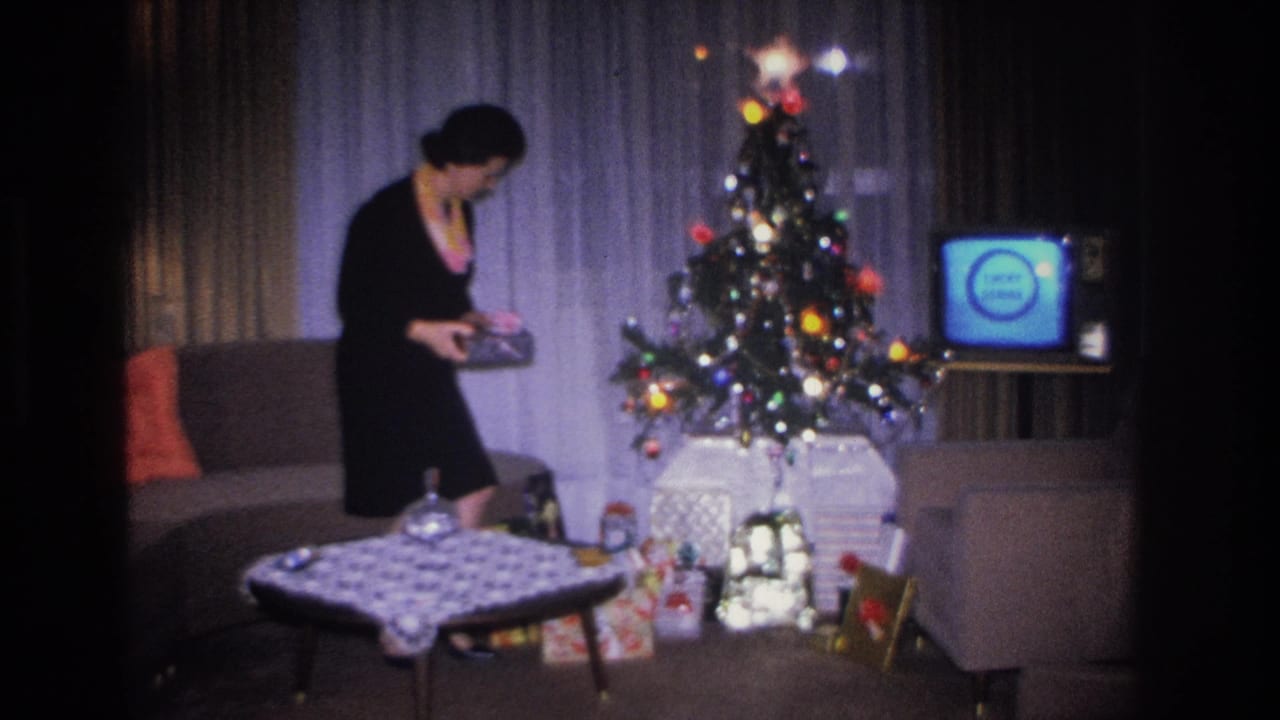 Woman in black dress standing by a Christmas tree examining a gift, with a vintage television showing a blue screen visible at right.