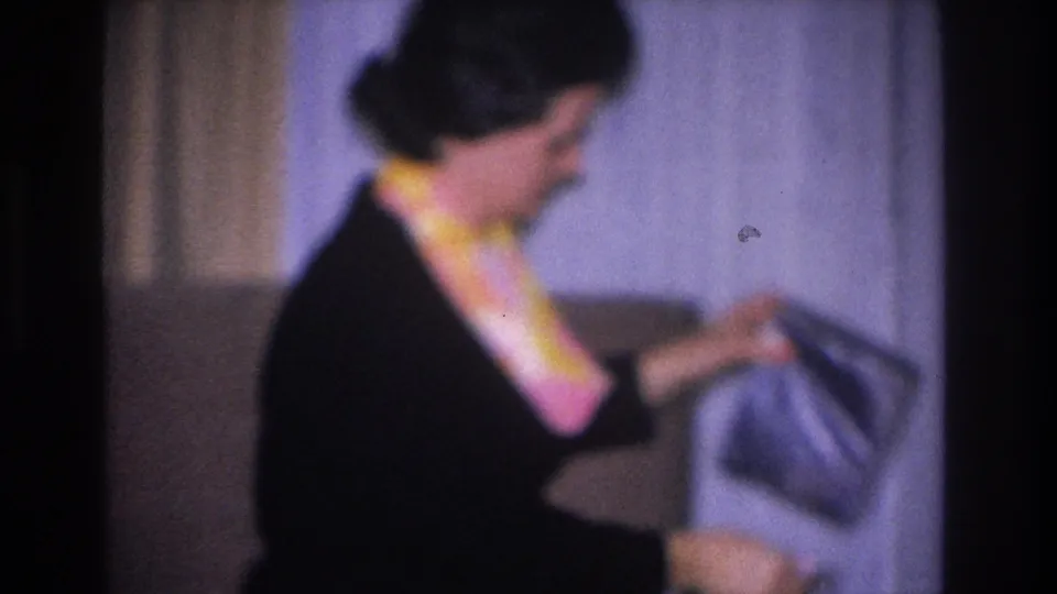 Close-up of woman removing what appears to be a dark fabric garment from a gift; circa 1966 8mm home movie attributed to Hoboken, New Jersey.