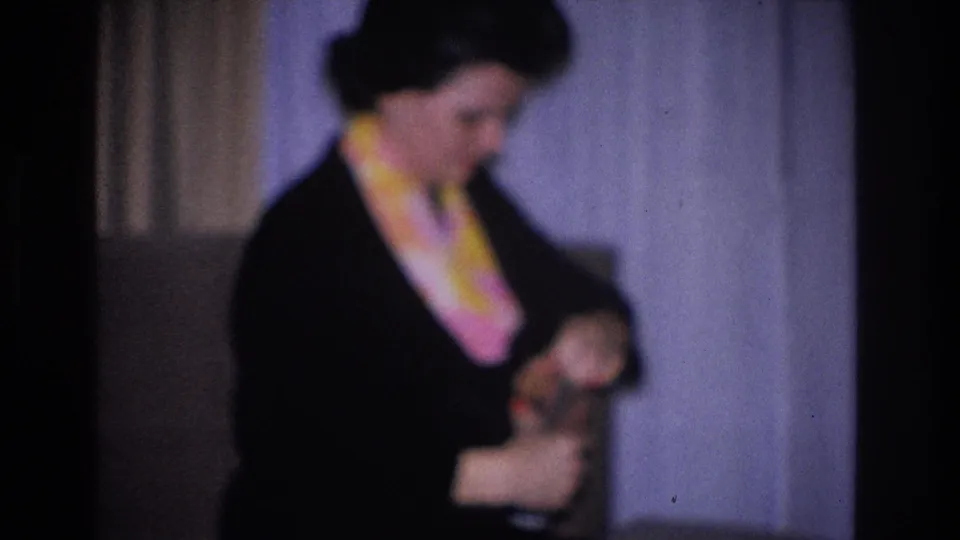 Woman in black dress and colorful scarf holding a small figurine or object; circa 1966 8mm home movie attributed to Hoboken, New Jersey.