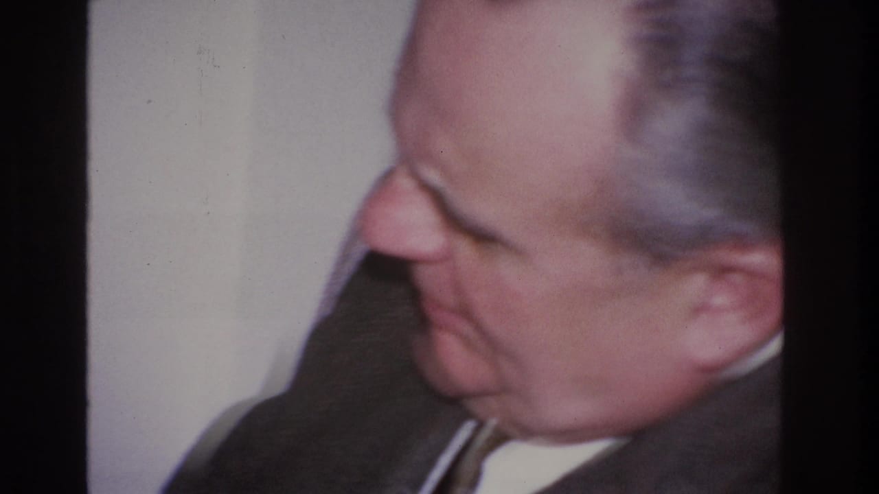 Close profile of a middle-aged man in dark business suit and narrow tie against a plain interior wall; home movie footage, Hoboken, New Jersey, circa 1966 per metadata.