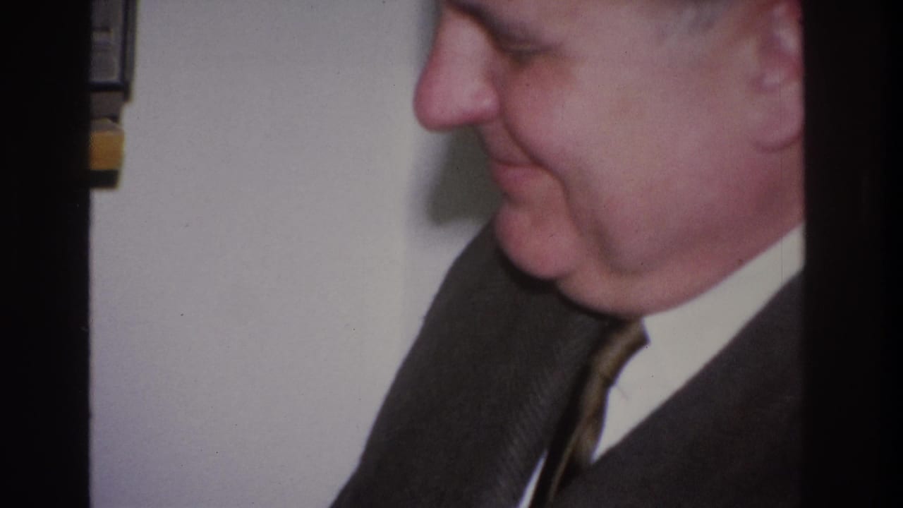 Close-up side profile of a middle-aged man in a dark charcoal suit and striped tie, 1966 8mm home movie, Hoboken, New Jersey.