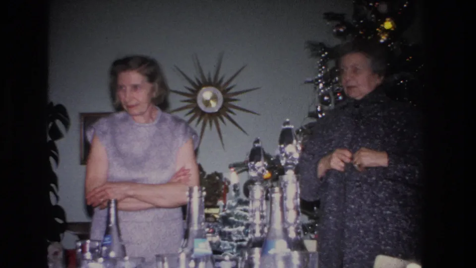 Two women in a mid-century living room with a starburst atomic-era wall clock and decorated Christmas tree; consistent with mid-1960s American domestic decor.