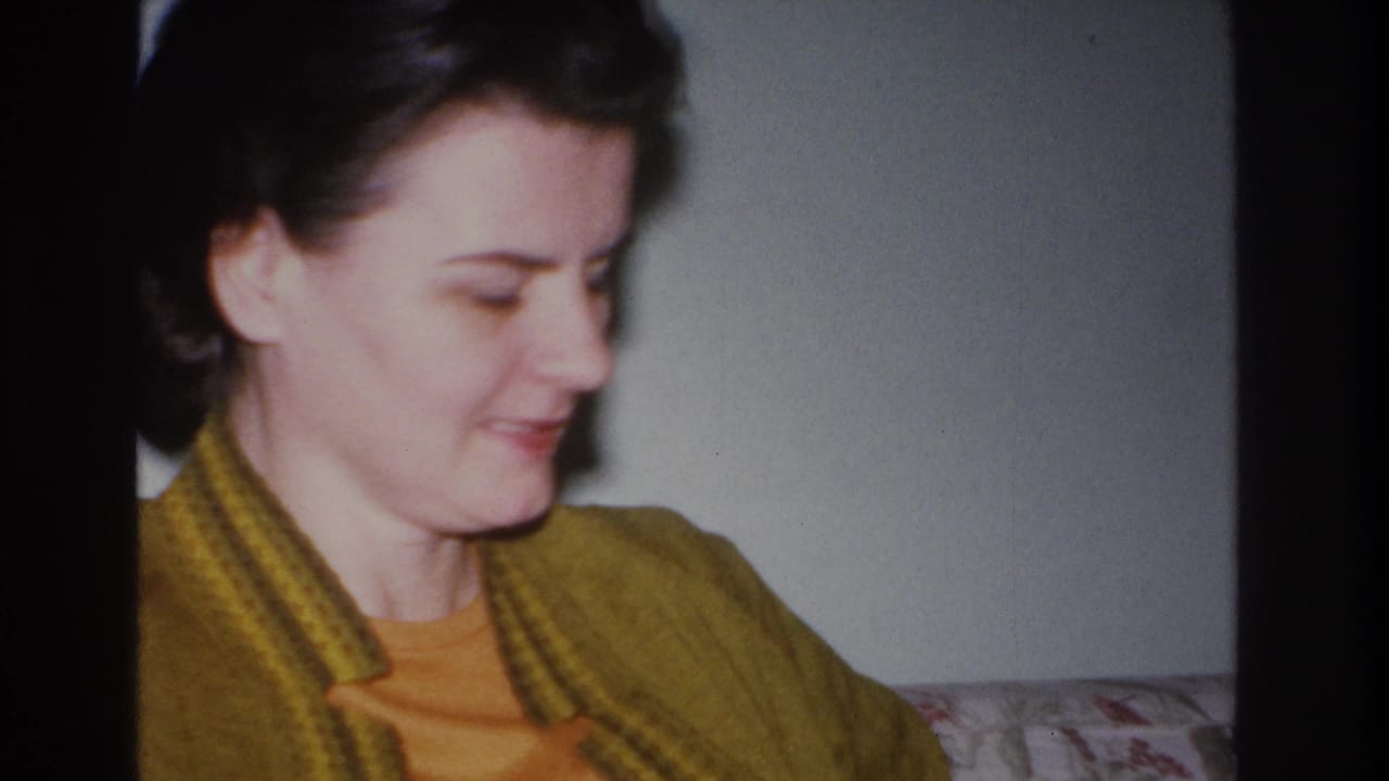 Medium close-up of the same dark-haired woman in mustard cardigan, now looking slightly downward; floral upholstery visible behind her.