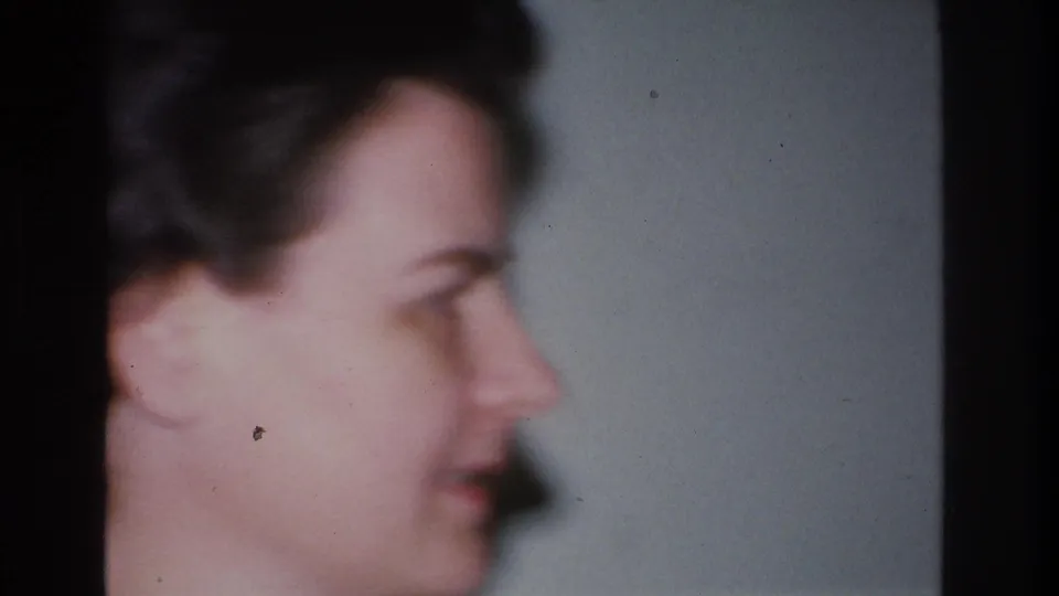 Extreme close-up profile of a woman with dark hair facing right; shallow focus and 8mm grain visible; consistent with Hoboken, New Jersey home movie, c. 1966.