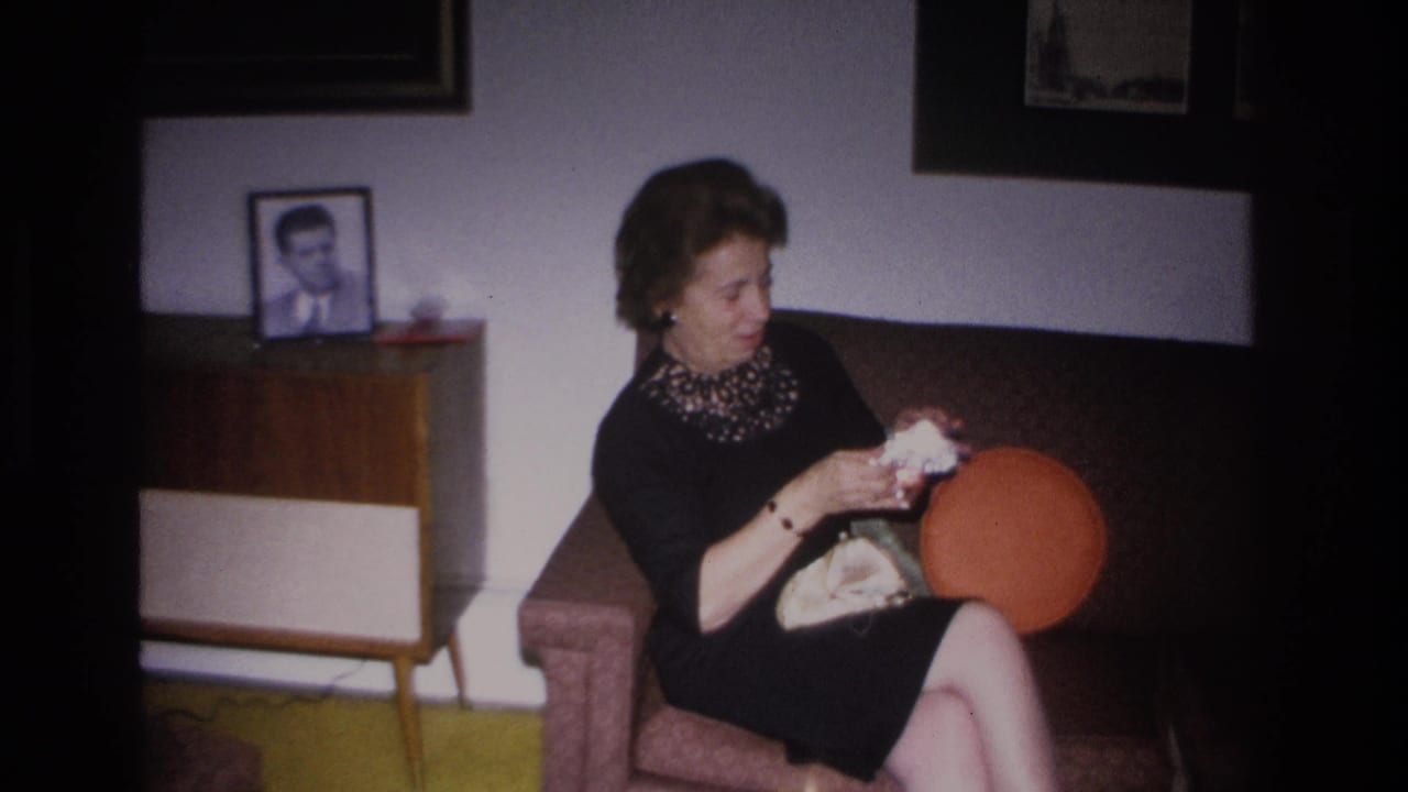 Mid-1960s woman seated in an armchair with open clutch purse; orange round pillow, mid-century sideboard, and framed man's portrait visible in Hoboken living room, circa 1966.
