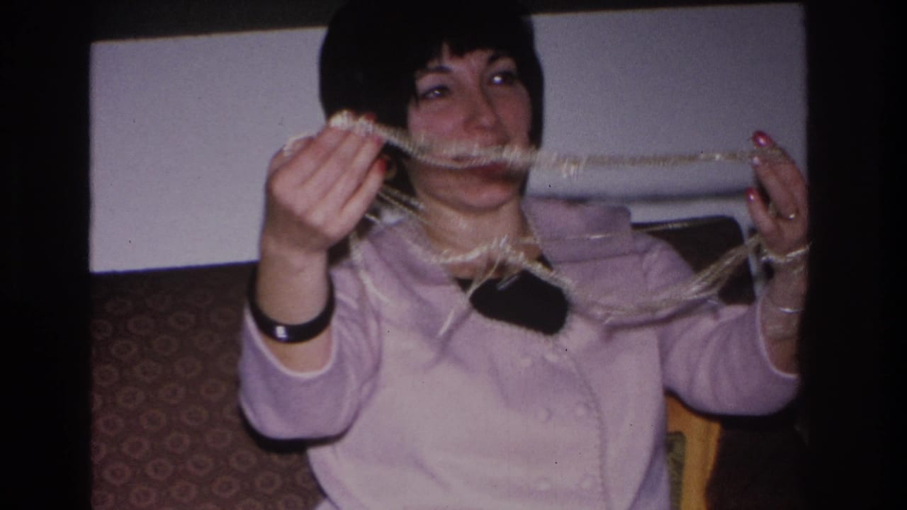 Woman in lavender cardigan holds a long beaded fringe string across her face; 8mm home movie, Hoboken NJ, 1966.