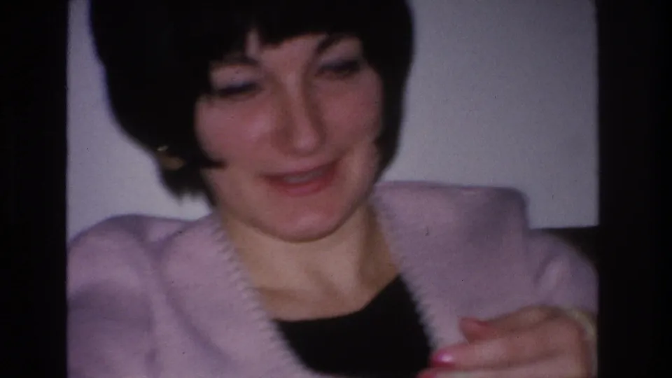 Close-up portrait of woman with short black bob and a quiet smile in lavender cardigan; 8mm home movie, Hoboken NJ, 1966.
