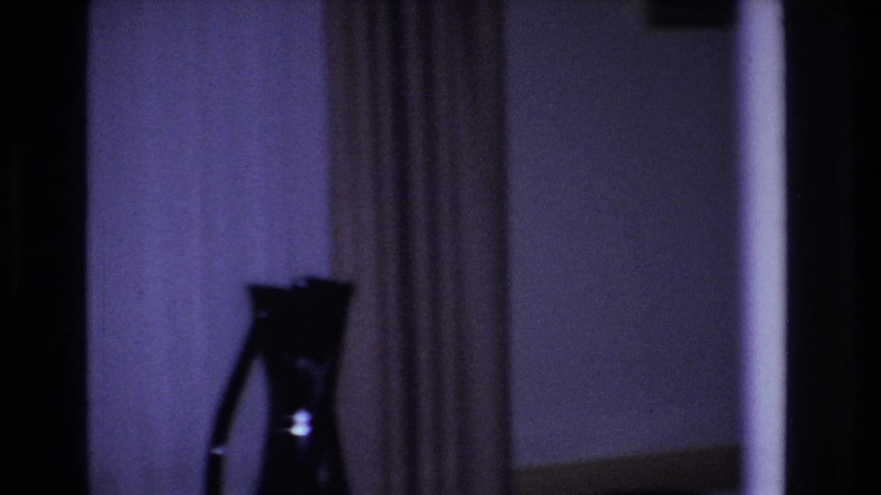 Opening 8mm frame from a 1966 Hoboken home movie: a dim living room with a pronounced purple dye-cast, a silhouetted tripod-mounted object, and floor-length drawn curtains.