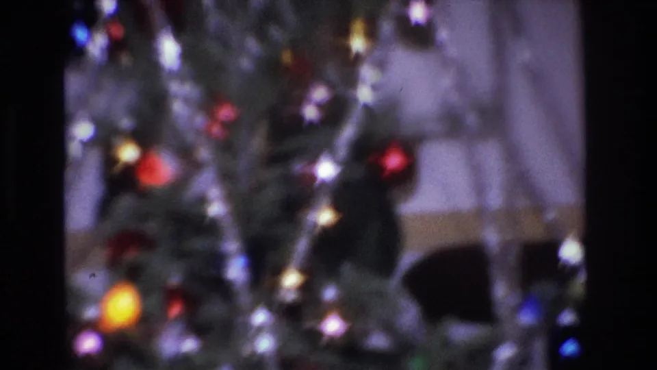 8mm close-up of a 1966 Christmas tree showing red and yellow glass ball ornaments, multicolored incandescent bulbs, and silver tinsel strands, with characteristic purple color cast from 1960s film aging.