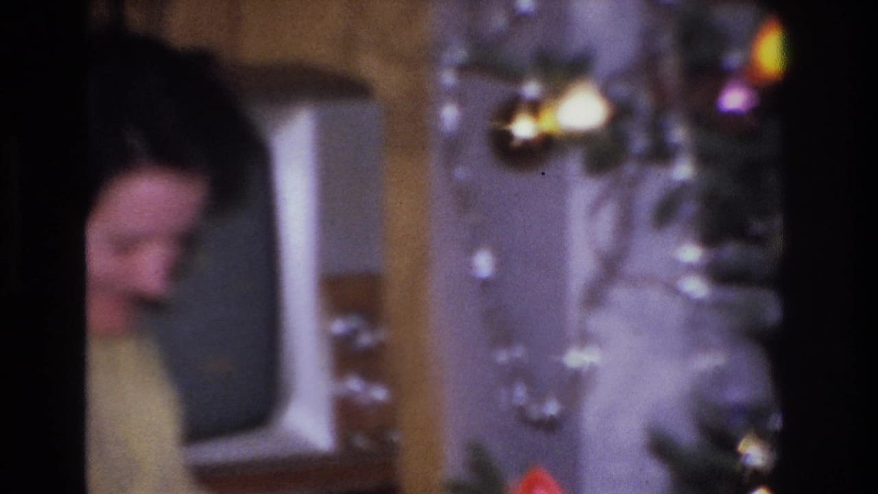 Dark-haired woman in pale yellow knit sweater near a decorated Christmas tree with large colored incandescent bulbs, Hoboken NJ, circa 1966, 8mm home movie