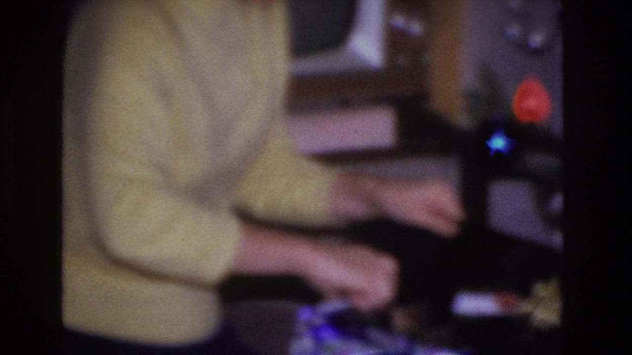 Woman's torso in yellow sweater handling a dark gift box, colored ornaments visible at right