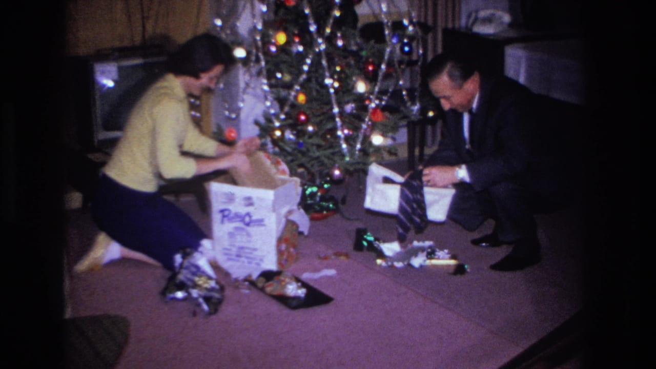 Adult couple opening Christmas presents on a purple carpet beside a multicolored-light tree in a private home interior, Hoboken, New Jersey, circa 1966.
