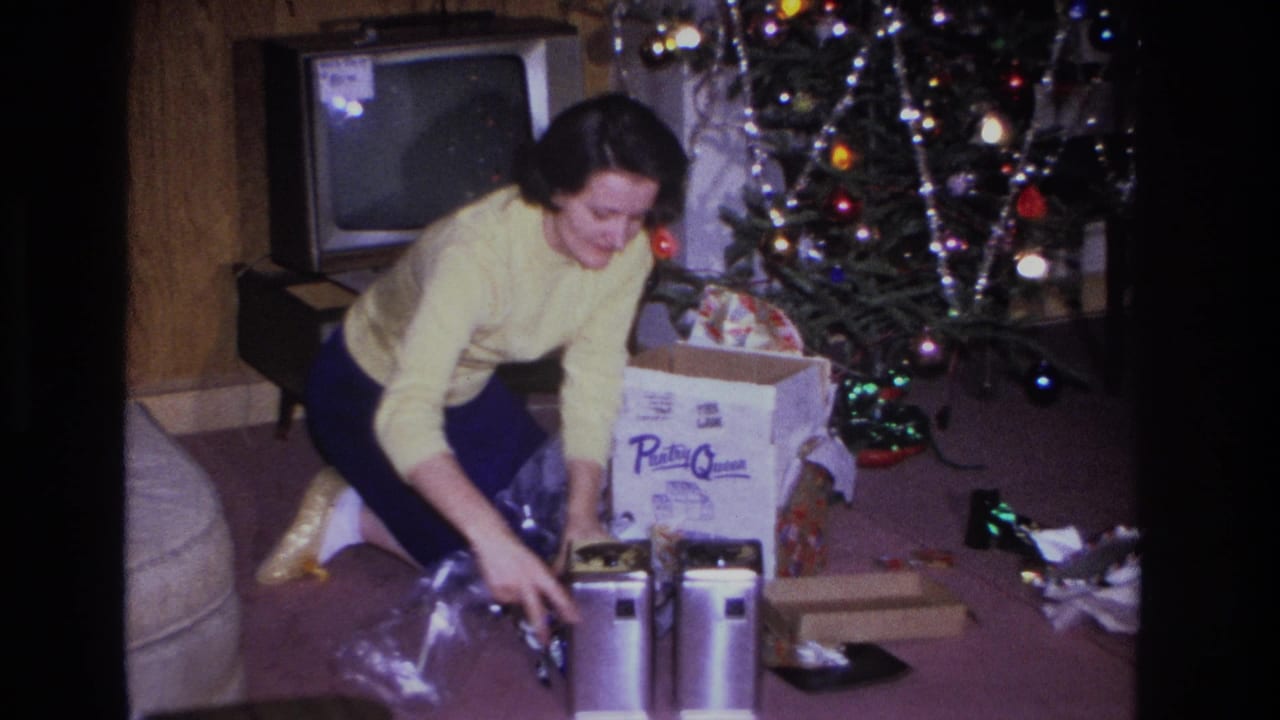 Mid-1960s Hoboken, NJ home movie showing a woman in a yellow sweater opening Christmas gifts beside a lit tree with tinsel and colored lights; CRT TV at left.