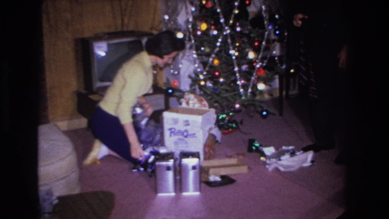 Woman in yellow sweater handles contents near a large cardboard box beside a Christmas tree with colored lights and silver icicles.